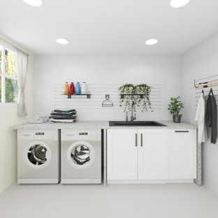 Klassisk inredning av en stor grå linjär grått tvättstuga enbart för tvätt, med en nedsänkt diskho, luckor med infälld panel, vita skåp, vita väggar, en tvättmaskin och torktumlare bredvid varandra och vitt stänkskydd