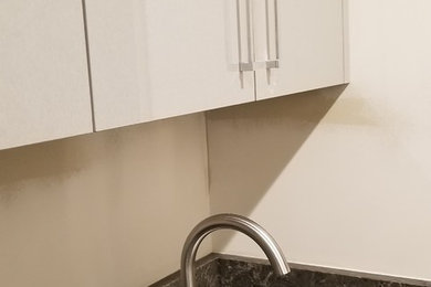 Photo of a small modern galley dedicated laundry room in Detroit with an undermount sink, flat-panel cabinets, grey cabinets, quartz benchtops, grey walls, limestone floors, a side-by-side washer and dryer, brown floor and brown benchtop.