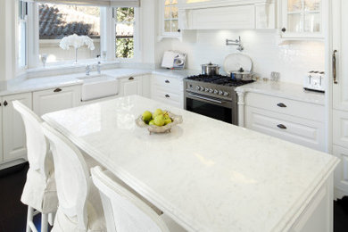Inspiration for a mid-sized traditional u-shaped eat-in kitchen in Sydney with a farmhouse sink, recessed-panel cabinets, marble benchtops, white splashback, subway tile splashback, stainless steel appliances, dark hardwood floors, multiple islands, black floor, white benchtop and recessed.