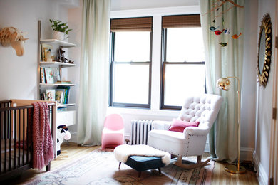 This is an example of a mid-sized transitional nursery for girls in New York with grey walls and light hardwood floors.