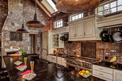 Example of a large mountain style l-shaped dark wood floor and brown floor open concept kitchen design in Denver with an integrated sink, raised-panel cabinets, beige cabinets, red backsplash, brick backsplash, paneled appliances, an island and black countertops
