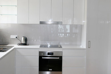 Contemporary kitchen in Wollongong with a double-bowl sink, flat-panel cabinets, white cabinets, white splashback and stainless steel appliances.
