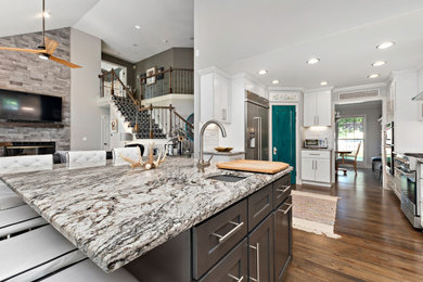 Mid-sized trendy l-shaped medium tone wood floor, brown floor and vaulted ceiling eat-in kitchen photo in Kansas City with an undermount sink, shaker cabinets, white cabinets, granite countertops, white backsplash, ceramic backsplash, stainless steel appliances, an island and white countertops
