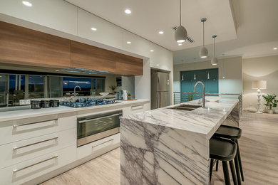 Design ideas for a large contemporary l-shaped open plan kitchen in Perth with an undermount sink, flat-panel cabinets, white cabinets, marble benchtops, black splashback, glass sheet splashback, stainless steel appliances, light hardwood floors and with island.