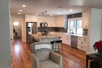 Mid-sized elegant l-shaped medium tone wood floor and brown floor open concept kitchen photo in Boise with a farmhouse sink, shaker cabinets, white cabinets, quartzite countertops, gray backsplash, subway tile backsplash, stainless steel appliances and an island