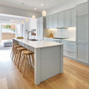 Bild på ett mellanstort maritimt vit linjärt vitt skafferi, med en enkel diskho, skåp i shakerstil, grå skåp, bänkskiva i koppar, vitt stänkskydd, rostfria vitvaror, mellanmörkt trägolv, en köksö och brunt golv