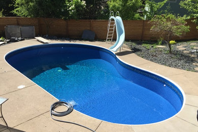 Diseño de piscina con tobogán clásica de tamaño medio tipo riñón en patio trasero con adoquines de hormigón