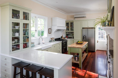 This is an example of a country kitchen in Perth with a farmhouse sink, shaker cabinets, green cabinets, quartz benchtops, white splashback, ceramic splashback, medium hardwood floors, with island and white benchtop.