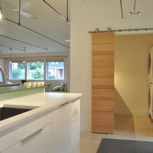 ボストンの小さいミッドセンチュリースタイルのおしゃれな家事室 (アンダーカウンターシンク、フラットパネル扉のキャビネット、白いキャビネット、人工大理石カウンター、白い壁、淡色無垢フローリング、上下配置の洗濯機・乾燥機) の写真