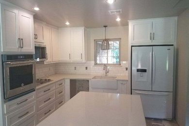 Eat-in kitchen - traditional eat-in kitchen idea in Oklahoma City with a farmhouse sink, shaker cabinets, white cabinets, white backsplash, subway tile backsplash, white appliances, an island and quartzite countertops