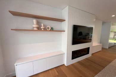 Diseño de sala de estar moderna grande con paredes blancas, suelo de madera clara, todas las chimeneas y televisor colgado en la pared