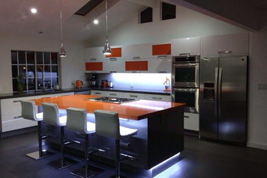 На фото: угловая кухня среднего размера в стиле модернизм с обеденным столом, двойной мойкой, белыми фасадами, столешницей из кварцевого агломерата, техникой из нержавеющей стали, плоскими фасадами и островом