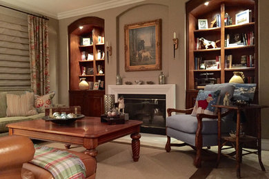 Example of a large classic enclosed travertine floor family room library design in San Diego with brown walls, a standard fireplace, a plaster fireplace and a concealed tv