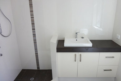 Inspiration for a small contemporary master bathroom in Perth with white tile, a drop-in sink, recessed-panel cabinets, white cabinets, laminate benchtops, a corner shower, ceramic tile, white walls and ceramic floors.