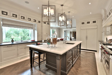 Large transitional u-shaped kitchen in Toronto with an undermount sink, recessed-panel cabinets, white cabinets, marble benchtops, stainless steel appliances, medium hardwood floors, with island and brown floor.