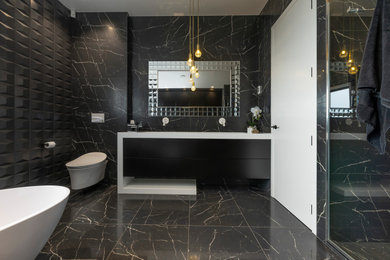 Photo of a mid-sized modern master bathroom in Auckland with flat-panel cabinets, black cabinets, a freestanding tub, a double shower, a wall-mount toilet, black tile, marble, black walls, marble floors, an undermount sink, solid surface benchtops, black floor, a hinged shower door, white benchtops, a double vanity and a floating vanity.