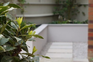 This is an example of a small contemporary courtyard partial sun garden in Kent with a retaining wall and natural stone paving.