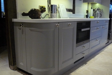 Photo of a transitional l-shaped eat-in kitchen in Sussex with a double-bowl sink, shaker cabinets, grey cabinets and black appliances.