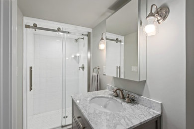 Photo of a mid-sized transitional 3/4 bathroom in New York with shaker cabinets, grey cabinets, an alcove shower, a one-piece toilet, white tile, subway tile, grey walls, an undermount sink, a sliding shower screen and grey benchtops.