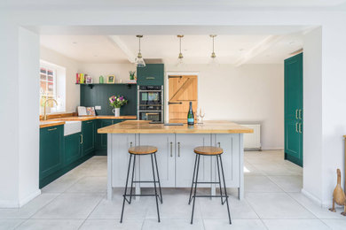 Design ideas for a small contemporary l-shaped open plan kitchen in Sussex with a farmhouse sink, shaker cabinets, green cabinets, black appliances, cement tiles, with island, grey floor, brown benchtop, recessed and wood benchtops.