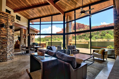 Large open concept family room in Phoenix with brown walls, a standard fireplace, a stone fireplace surround, a built-in media wall and travertine floors.