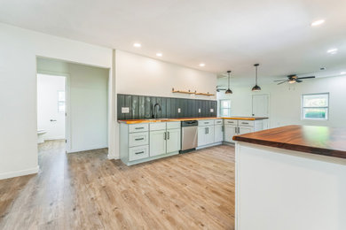 Mid-sized cottage vinyl floor and brown floor eat-in kitchen photo in Little Rock with a drop-in sink, shaker cabinets, gray cabinets, wood countertops, black backsplash, wood backsplash, stainless steel appliances, a peninsula and brown countertops