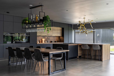 Inspiration for an expansive industrial grey and black single-wall open plan kitchen in Other with a built-in sink, flat-panel cabinets, black cabinets, engineered stone countertops, brown splashback, stone slab splashback, black appliances, ceramic flooring, an island, black worktops, a drop ceiling and feature lighting.