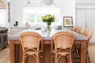 Example of a classic light wood floor and beige floor kitchen design in New York with white cabinets, marble countertops, white backsplash, subway tile backsplash and an island