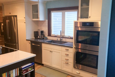 Small trendy single-wall medium tone wood floor kitchen photo in Boston with an undermount sink, recessed-panel cabinets, white cabinets, white backsplash, subway tile backsplash, stainless steel appliances, an island and granite countertops