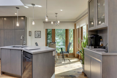 Mid-sized trendy u-shaped medium tone wood floor and brown floor eat-in kitchen photo in Calgary with an undermount sink, flat-panel cabinets, gray cabinets, solid surface countertops, blue backsplash, mosaic tile backsplash, stainless steel appliances, an island and gray countertops