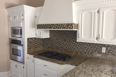 Example of a mid-sized transitional l-shaped vinyl floor eat-in kitchen design in New Orleans with recessed-panel cabinets, white cabinets, granite countertops, brown backsplash, mosaic tile backsplash, stainless steel appliances and a peninsula
