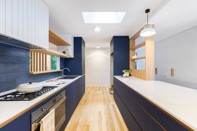 Design ideas for a mid-sized contemporary galley kitchen pantry in Canberra - Queanbeyan with a drop-in sink, blue cabinets, quartz benchtops, blue splashback, cement tile splashback, stainless steel appliances, medium hardwood floors and white benchtop.