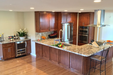 Mid-sized elegant u-shaped light wood floor and beige floor open concept kitchen photo in San Francisco with an undermount sink, shaker cabinets, medium tone wood cabinets, granite countertops, beige backsplash, stone tile backsplash, stainless steel appliances, a peninsula and brown countertops