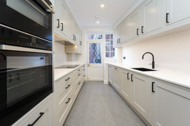 Design ideas for a mid-sized traditional galley kitchen in London with a drop-in sink, shaker cabinets, white cabinets, quartzite benchtops, stainless steel appliances, porcelain floors, no island, multi-coloured floor and white benchtop.