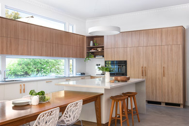 This is an example of a medium sized contemporary l-shaped kitchen/diner in Perth with medium wood cabinets, engineered stone countertops, white splashback, black appliances, concrete flooring, an island and white worktops.