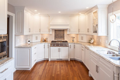 Mid-sized transitional u-shaped medium tone wood floor eat-in kitchen photo in Other with an undermount sink, raised-panel cabinets, white cabinets, granite countertops, beige backsplash, porcelain backsplash, paneled appliances and no island