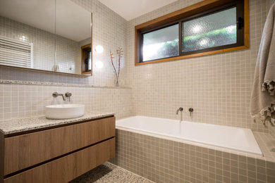 Mid-sized midcentury kids bathroom in Geelong with flat-panel cabinets, medium wood cabinets, a drop-in tub, beige tile, ceramic tile, beige walls, terrazzo floors, a vessel sink, terrazzo benchtops, multi-coloured floor, a single vanity and a floating vanity.