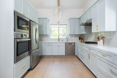 Example of a mid-sized trendy u-shaped light wood floor and vaulted ceiling eat-in kitchen design in San Francisco with an undermount sink, shaker cabinets, blue cabinets, quartz countertops, white backsplash, quartz backsplash, stainless steel appliances, no island and white countertops