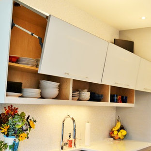 Aménagement d'une grande arrière-cuisine contemporaine en L avec un évier encastré, un placard à porte vitrée, des portes de placard en bois clair, un plan de travail en verre, une crédence blanche, une crédence en carreau de verre, un électroménager en acier inoxydable, un sol en bois clair et un îlot central.