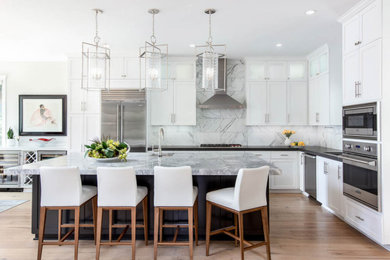 Example of a large minimalist l-shaped light wood floor and brown floor eat-in kitchen design in San Diego with flat-panel cabinets, white cabinets, quartz countertops, gray backsplash, ceramic backsplash, stainless steel appliances, an island and black countertops