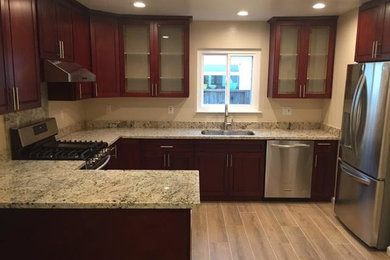 Eat-in kitchen - mid-sized traditional u-shaped light wood floor and beige floor eat-in kitchen idea in San Francisco with raised-panel cabinets, dark wood cabinets, granite countertops, stainless steel appliances and a peninsula