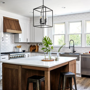 Example of a mid-sized transitional u-shaped medium tone wood floor and brown floor eat-in kitchen design in DC Metro with stainless steel appliances, an island, a farmhouse sink, shaker cabinets, white cabinets, quartz countertops, white backsplash and gray countertops