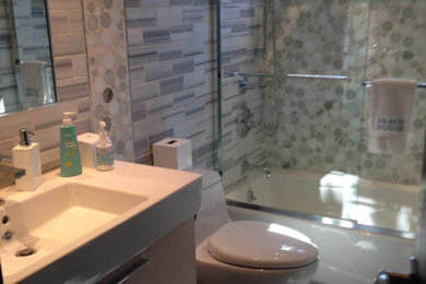 Bathroom - mid-sized modern 3/4 gray tile and glass tile porcelain tile bathroom idea in New York with an integrated sink, flat-panel cabinets, light wood cabinets, solid surface countertops, a one-piece toilet and gray walls