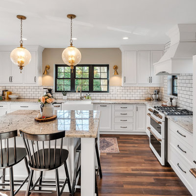 Inspiration for a timeless l-shaped dark wood floor and brown floor kitchen remodel in Detroit with a farmhouse sink, recessed-panel cabinets, white cabinets, white backsplash, subway tile backsplash, white appliances, an island and gray countertops