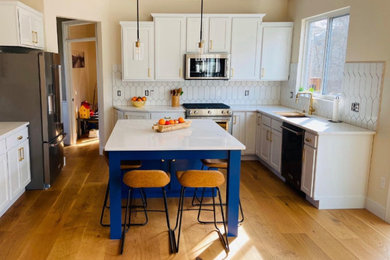 Example of a mid-sized transitional u-shaped light wood floor and brown floor eat-in kitchen design with a single-bowl sink, shaker cabinets, white cabinets, quartz countertops, white backsplash, ceramic backsplash, stainless steel appliances, an island and white countertops
