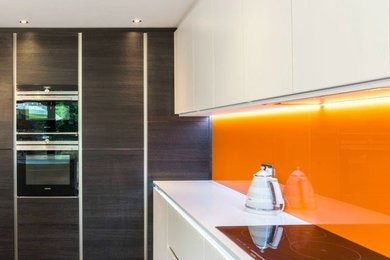Diseño de cocina moderna de tamaño medio con armarios con paneles lisos, puertas de armario blancas, encimera de cuarcita, salpicadero naranja, salpicadero de vidrio templado, una isla y encimeras blancas