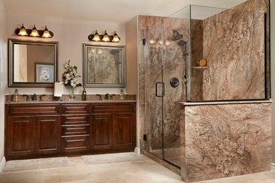 Photo of a mid-sized traditional master bathroom in San Diego with raised-panel cabinets, dark wood cabinets, a corner shower, beige tile, stone slab, beige walls, porcelain floors, an undermount sink, solid surface benchtops, beige floor and a hinged shower door.