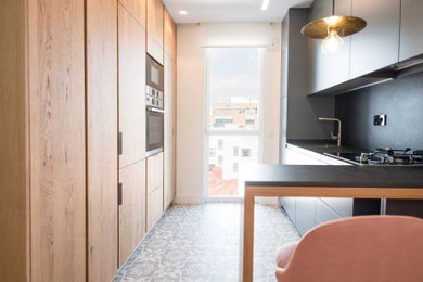 Example of a mid-sized minimalist u-shaped ceramic tile and gray floor open concept kitchen design in Madrid with a drop-in sink, flat-panel cabinets, light wood cabinets, quartz countertops, black backsplash, quartz backsplash, paneled appliances, a peninsula and black countertops