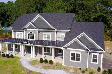 Imagen de fachada de casa gris actual grande de dos plantas con revestimiento de aglomerado de cemento, tejado a dos aguas y tejado de teja de madera