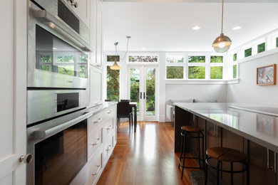 Inspiration for a mid-sized craftsman medium tone wood floor eat-in kitchen remodel in Seattle with a farmhouse sink, shaker cabinets, white cabinets, quartz countertops, blue backsplash, subway tile backsplash, stainless steel appliances, an island and white countertops